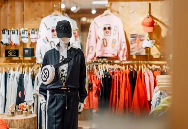 A fashionable mannequin with a black outfit and a hat in a store. In the background, colorful clothing and accessories can be seen.