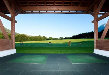 A view of a large golf practice area with a clear blue sky. In the foreground, there is a covered area with mats.