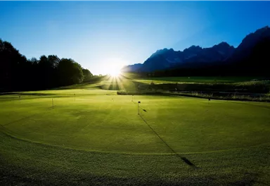 A beautiful golf course landscape at sunrise. The mountains in the background and the green grass create a serene atmosphere.