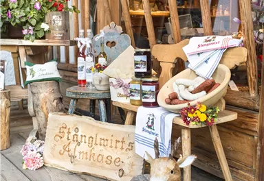 Eine rustikale Marktbude mit Holzdekoration und regionalen Produkten. Auf einem Holztisch stehen Marmelade, Käse und eine dekorative Figur eines Rehs.