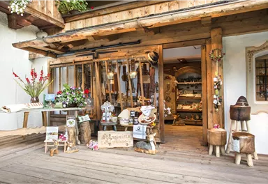 Ein rustikaler Laden mit Holzverzierungen und einer einladenden Schaufensterdekoration. Vor der Tür stehen Pflanzen und handgefertigte Artikel zum Verkauf.