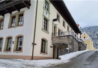 Ein malerisches Gebäude in den Bergen, umgeben von Schnee. Die Architektur ist traditionell mit Holzverzierungen und großen Fenstern.