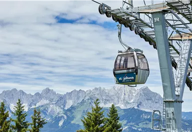 A cable car glides over an impressive mountain landscape. The sky is cloudy, and the mountains in the background are majestic.