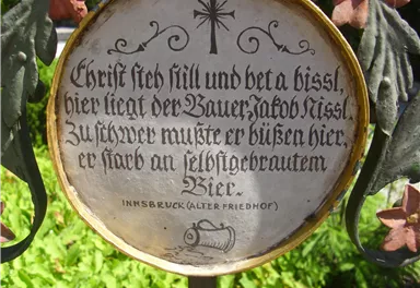 A metal memorial plaque with an inscription in old German script. The plaque commemorates a deceased farmer and is located in a cemetery.