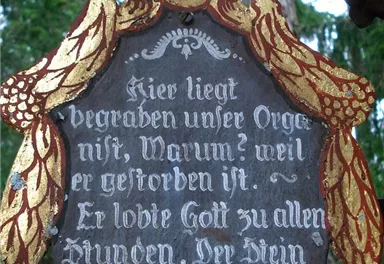 A decorated tombstone with a poetic inscription. The surroundings consist of trees and a tranquil natural backdrop.