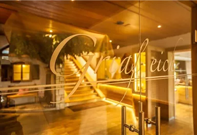 Ein einladender Eingangsbereich mit einer stilvollen Glastür. Im Hintergrund sind eine Treppe und warmes Licht sichtbar.