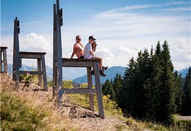 A beautiful view from a wooden platform in the mountains. Two people are sitting on the platform, enjoying the landscape.