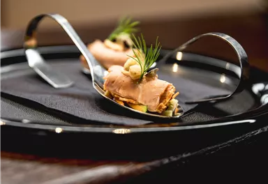 Ein elegantes Gericht auf einem schwarzen Teller. Die Präsentation umfasst zarte Zutaten und dekorative Kräuter.