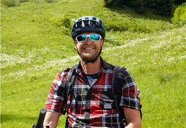 A cheerful cyclist on a green path. In the background, trees and a picturesque landscape can be seen.