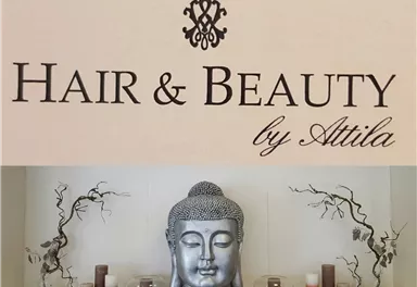 A stylish sign with the inscription "Hair & Beauty by Attila". Below it stands a Buddha statue, surrounded by decorative candles and branches.