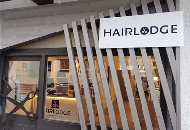 Ein Friseursalon namens "HAIRLODGE" mit einer modernen Fassade und großen Fenstern. Das Schild hebt den Namen des Salons hervor.