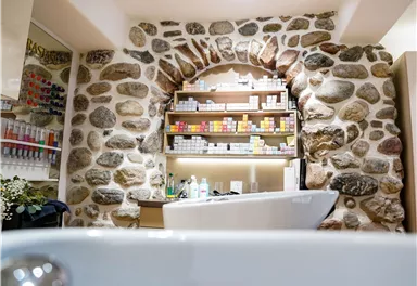 An elegant room with a stone wall and shelves full of care products. In the foreground, a bathtub is visible.