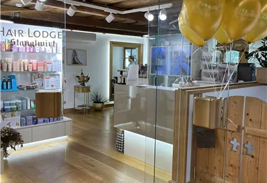 A modern hair salon with an elegant reception area and colorful balloons. The shelves are filled with various hair care products.