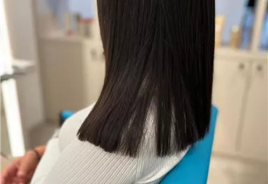 Eine Person mit glattem, langem Haar sitzt in einem Friseursalon. Die Rückansicht zeigt einen modernen Look.