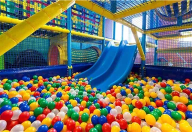 A colorful play area with slides and a ball pit. The floor is filled with many colorful balls in various colors.