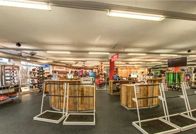 A well-lit sports store with wooden tables and a variety of sports items. Shelves are filled with equipment and clothing.