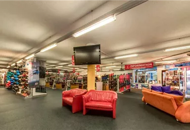 A spacious sales area with shelves full of sports goods. Comfortable seating and a large screen create an inviting atmosphere.