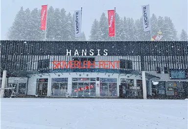 A ski rental named "Hansis" in the snow. The facade is modern, surrounded by snow-covered trees.