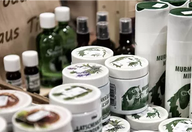 Eine Vielzahl von Naturprodukten in verschiedenen Verpackungen ist zu sehen. Die Artikel sind hauptsächlich in weißen und grünen Tönen gehalten und beinhalten Cremes, Öle und andere Pflegeprodukte.