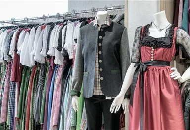 Eine Auswahl traditioneller Trachtenbekleidung ist zu sehen. Mode in verschiedenen Farben und Stilen hängt an Kleiderstangen.