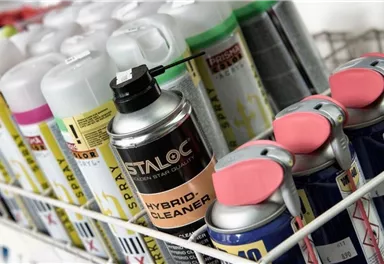 Eine Reihe von Spraydosen in einem Regal. Die Dosen sind in verschiedenen Farben und mit unterschiedlichen Etiketten beschriftet.