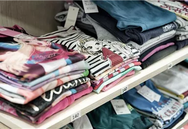 Bunte T-Shirts sind ordentlich auf Regalen gestapelt. Einige haben Aufdrucke und Preisschilder.