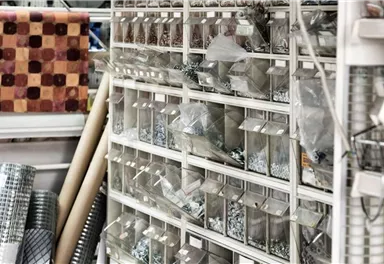 Ein Regal mit verschiedenen Behältern, die Schrauben und andere Kleinteile enthalten. Im Hintergrund sind mehr Materialien für Bau- und Bastelarbeiten zu sehen.