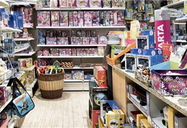Ein bunter Spielwarenladen mit Regalen voller Spielzeuge und Plüschtiere. In der Mitte steht ein Korb mit weiteren Spielzeugen.