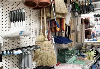 Ein Geschäft mit verschiedenen Reinigungswerkzeugen und Zubehör. An der Wand hängen Besen, Schaufeln und andere Haushaltsartikel.