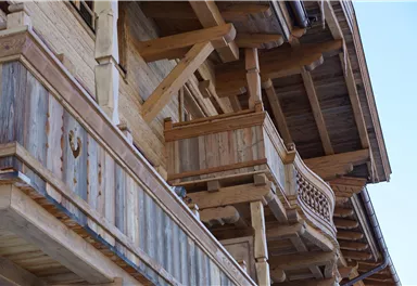 Ein traditionelles Holzgebäude mit Balkonen und sichtbaren Holzbalken. Das Dach ist stilvoll gestaltet und verleiht dem Gebäude einen rustikalen Charme.