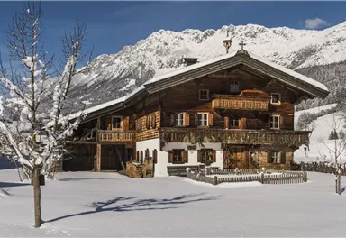 A cozy wooden house in the snow with a picturesque mountain panorama. The landscape is calm and wintry, with snow-covered trees.