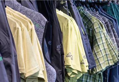 Ein Sortiment an Freizeitkleidung hängt in einem Geschäft. Die Auswahl umfasst T-Shirts und Hosen in verschiedenen Farben und Mustern.