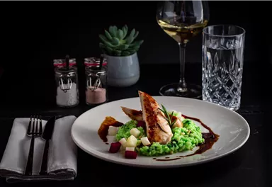 A beautiful dish with fried chicken on a bed of green risotto. Accompanied by fine vegetable cubes and a small portion of sauce.