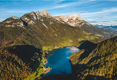 Eine atemberaubende Berglandschaft mit schneebedeckten Gipfeln und einem klaren See im Vordergrund. Die Natur ist umgeben von grünen Wäldern und Feldern.
