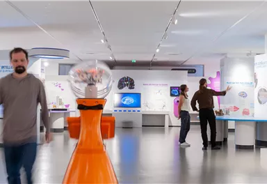 A modern museum with interactive exhibits. People explore various stations in a bright and open space.