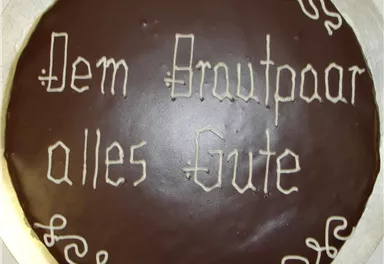 A pretty cake with chocolate icing and decorative writing. It is adorned with the wish "Wishing the couple all the best."