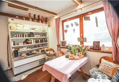 A cozy room with a table and a shelf wall full of food. Large windows let in plenty of light and decorative details create an inviting atmosphere.