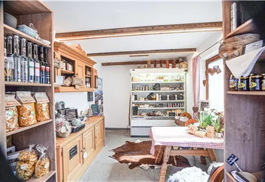 A cozy store with shelves full of food and homemade products. In the middle stands a table with a checkered tablecloth and fresh plants.