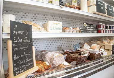 A display shelf with various food items, including baked goods and pickled products. A sign explains the products and their origin.