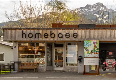 A store named "homebase" in a picturesque setting. Snow-capped mountains are visible in the background.