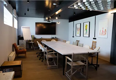 A modern meeting room with a large table, chairs, and colorful wall murals. The room is well-lit and provides a pleasant atmosphere for meetings.