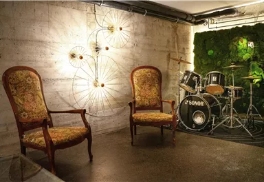 A stylish room with two elegant chairs and a small drum set corner. The wall is designed with artificial moss and decorative lights.