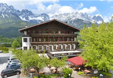 Ein charmantes Hotel inmitten der Berge, umgeben von Bäumen und Blumen. Die alpine Landschaft bietet eine malerische Kulisse.