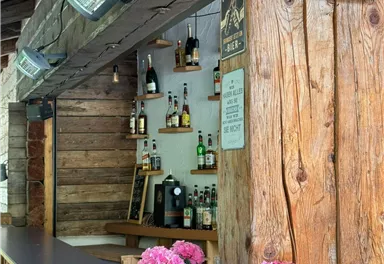 A cozy bar with wood paneling and a counter. On the table are two flower boxes with pink flowers.
