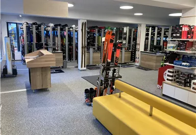 A modern ski shop with shelves full of ski equipment. In the foreground is a yellow sofa and a reception counter.