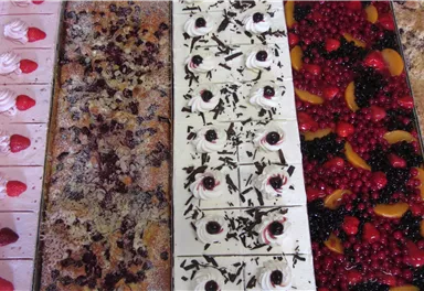 A tray full of colorful desserts, including cream cakes and fruity sheet cakes. The treats are visually appealing and range from strawberries to various fruit toppings.