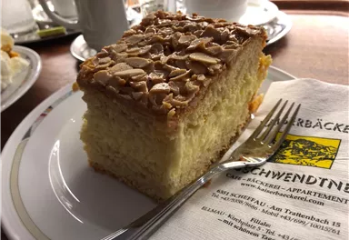 A piece of cake with a crispy almond layer on a plate. Next to it lies a fork and a napkin piece.