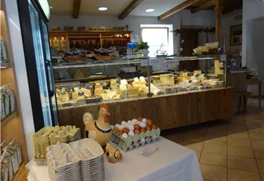 A cheese shop with a large selection of cheese varieties. In the foreground, there are eggs and a decorative chicken.