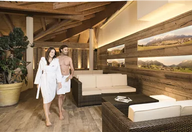 A modern spa with wood-paneled walls and cozy seating areas. A couple in bathrobes enjoys the relaxing atmosphere.