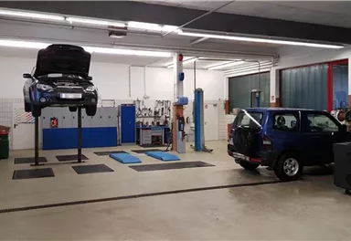 A workshop with two cars, one is on a lift. The floor is clean and the walls are bright.